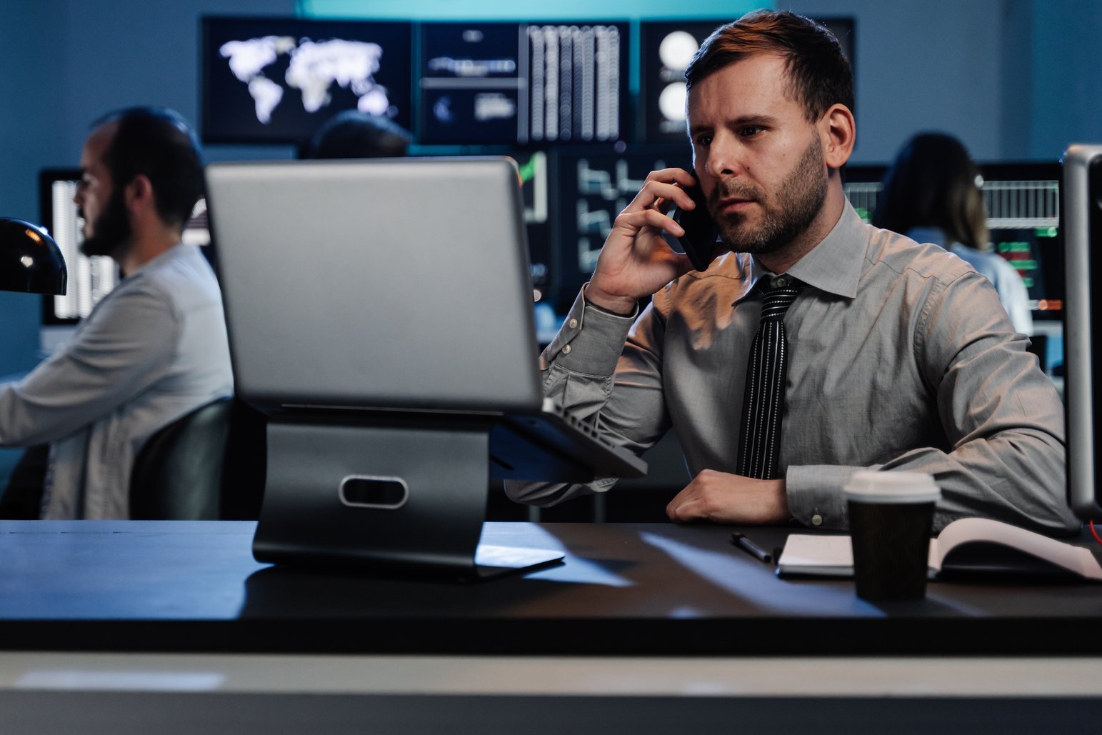 Successful trader businessman on a phone call investing in stock market using computer screens in busy modern office